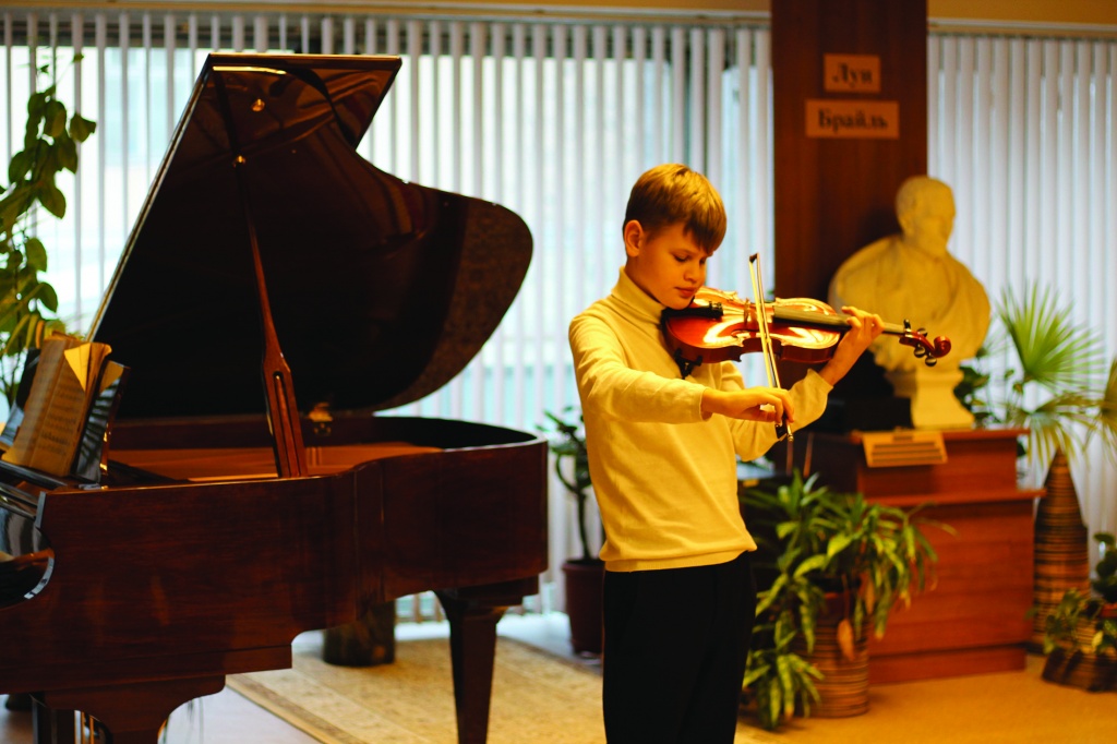 Young violinist on the background of the bust of Louis Braille